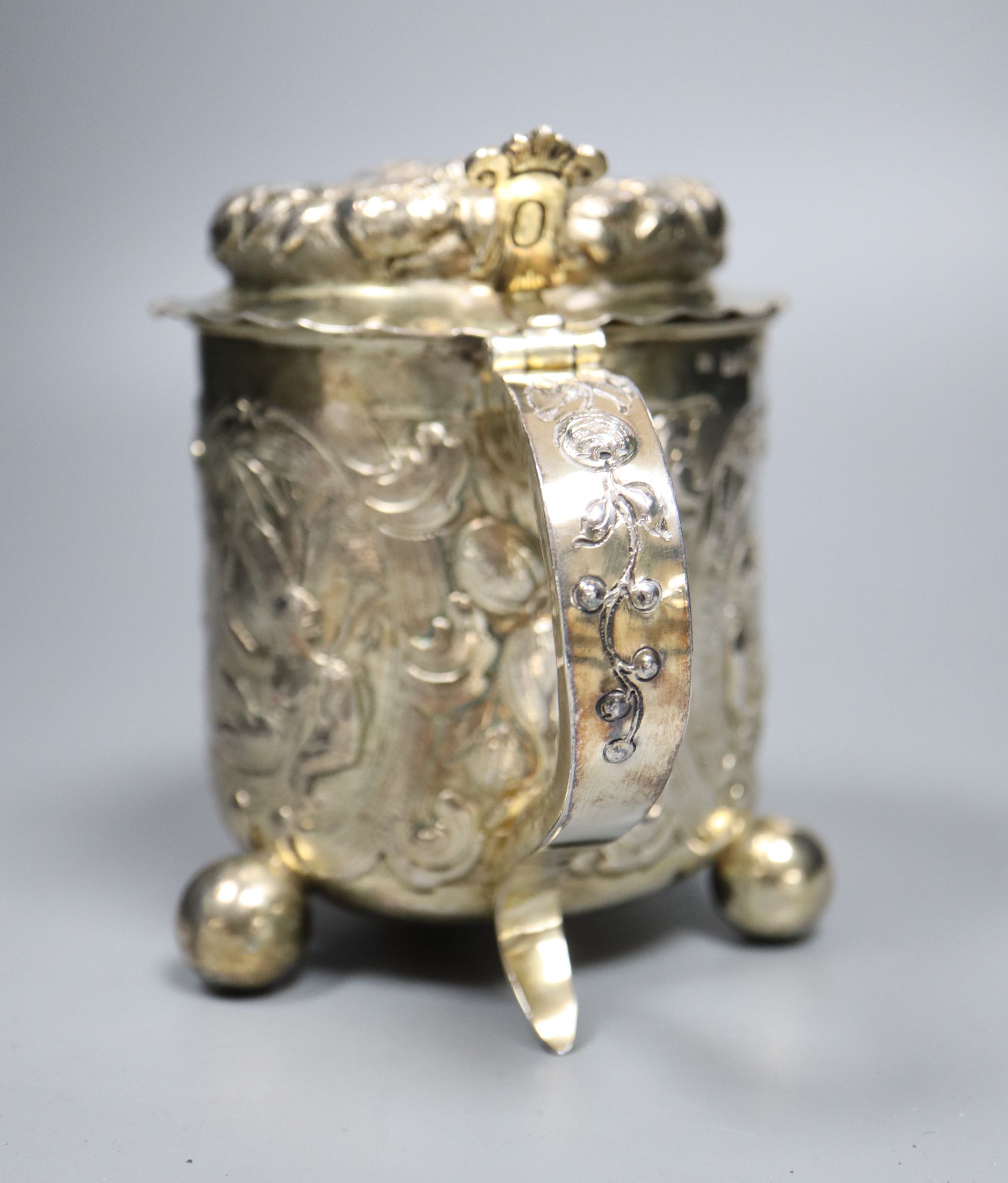 A late 19th century German? silver Scandinavian style embossed lidded tankard, on three ball feet,